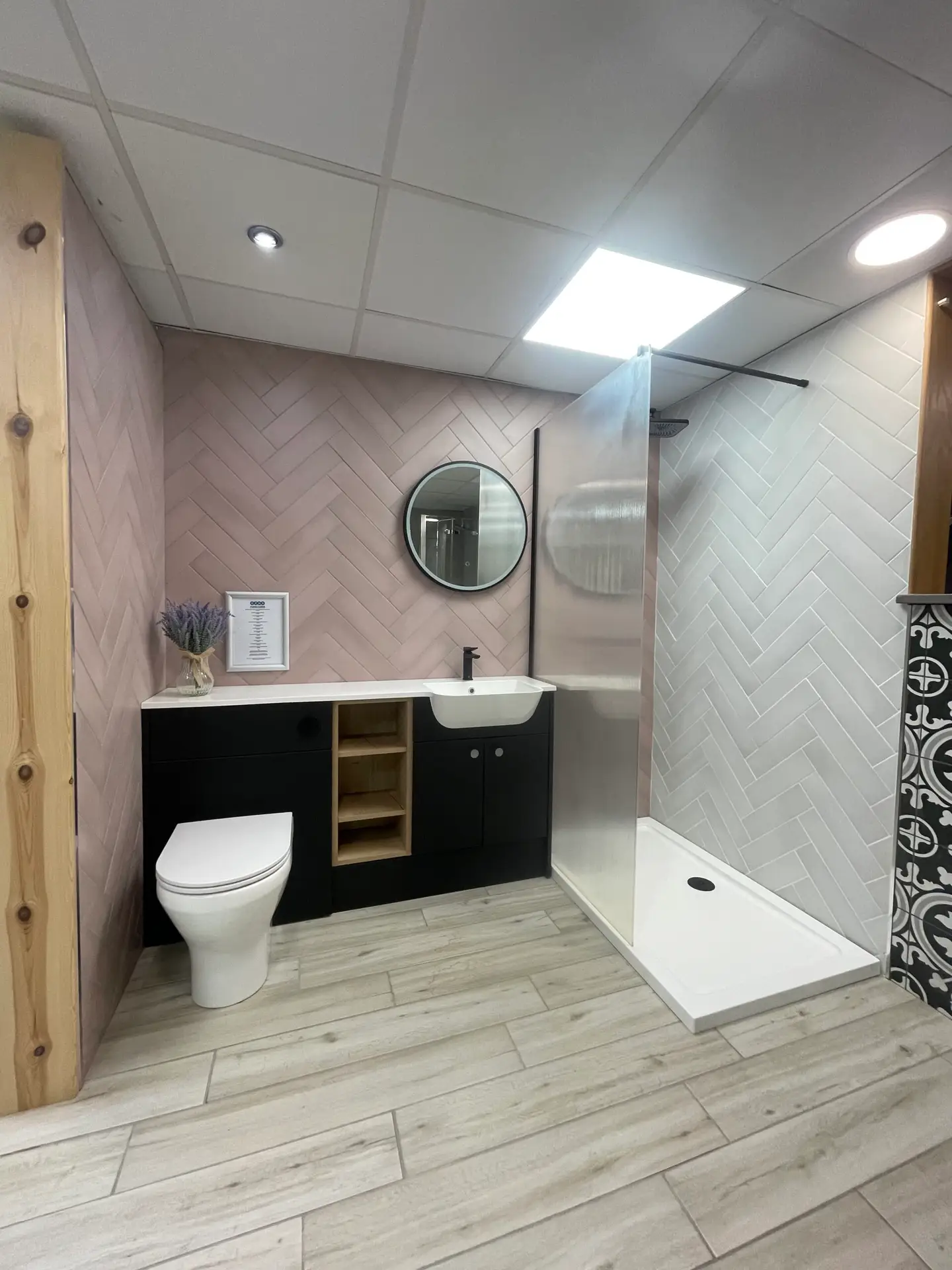 black furniture run with round mirror, shower tray and herringbone tiles in pink and white